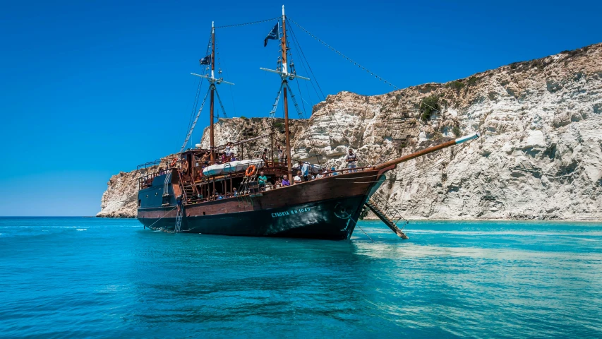 large wooden boat with people on the deck floating near shore