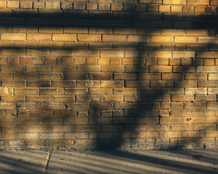 the shadows of two benches and a lamp against a stone wall