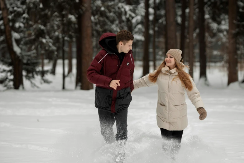 a woman and man walking through a snow covered forest