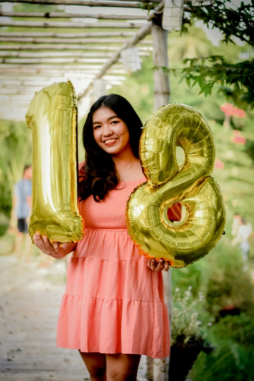a woman holds up gold balloons to spell the number eighteen