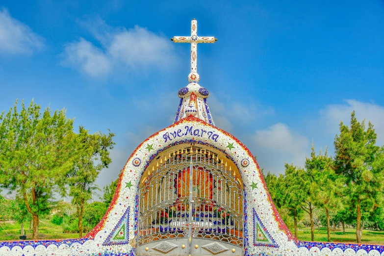 a beautiful cross stands near a church with many colorful glass mosaics on it