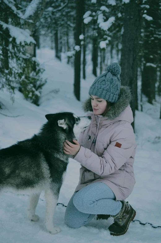 a woman kneeling down in the snow petting her dog