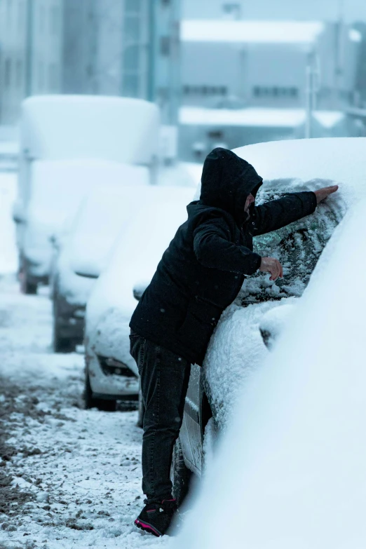 a person standing in the snow next to parked cars