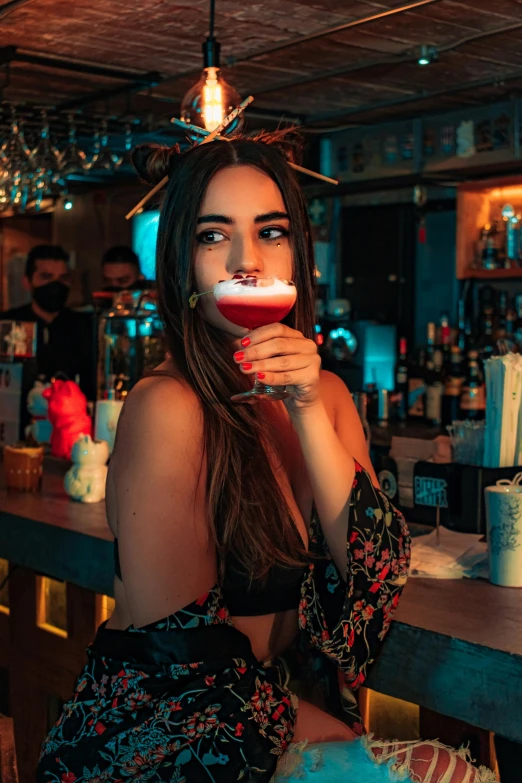 a beautiful young woman drinking a beer in front of a bar counter