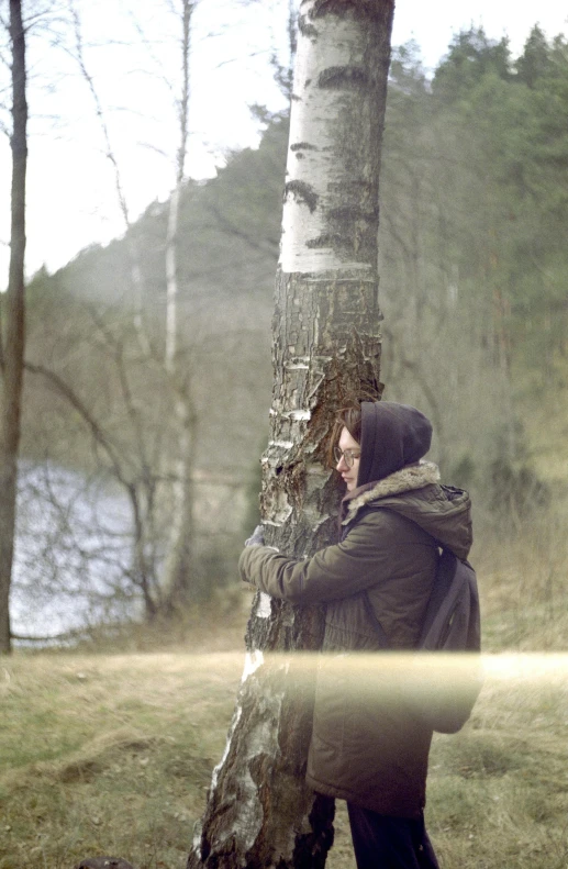 a man stands next to a tree in the woods