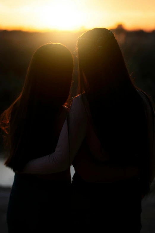 two girls are seen emcing each other as the sun rises in the background