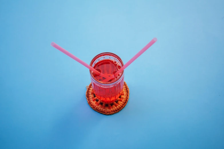 two plastic straws with one straw sticking out, and another straw inside, sitting on a wooden basket holding a red glass