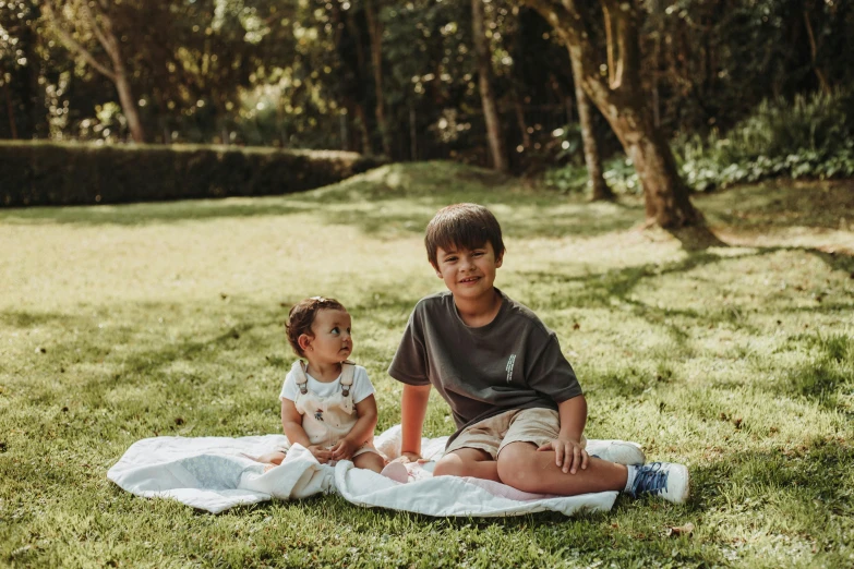 two children are sitting on a blanket in a field