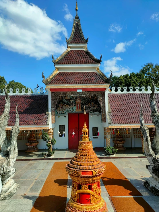 a building with a red door and roof with a statue on the ground