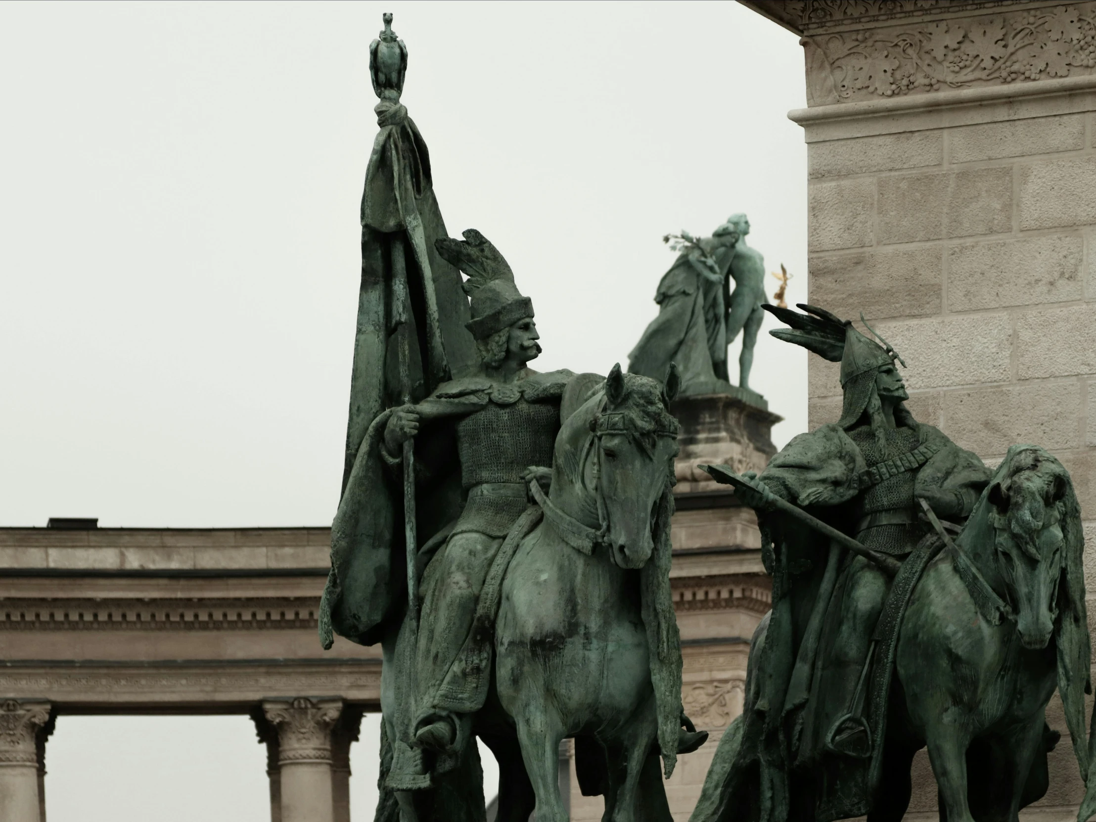 bronze statues stand near a stone pillar of a historical building