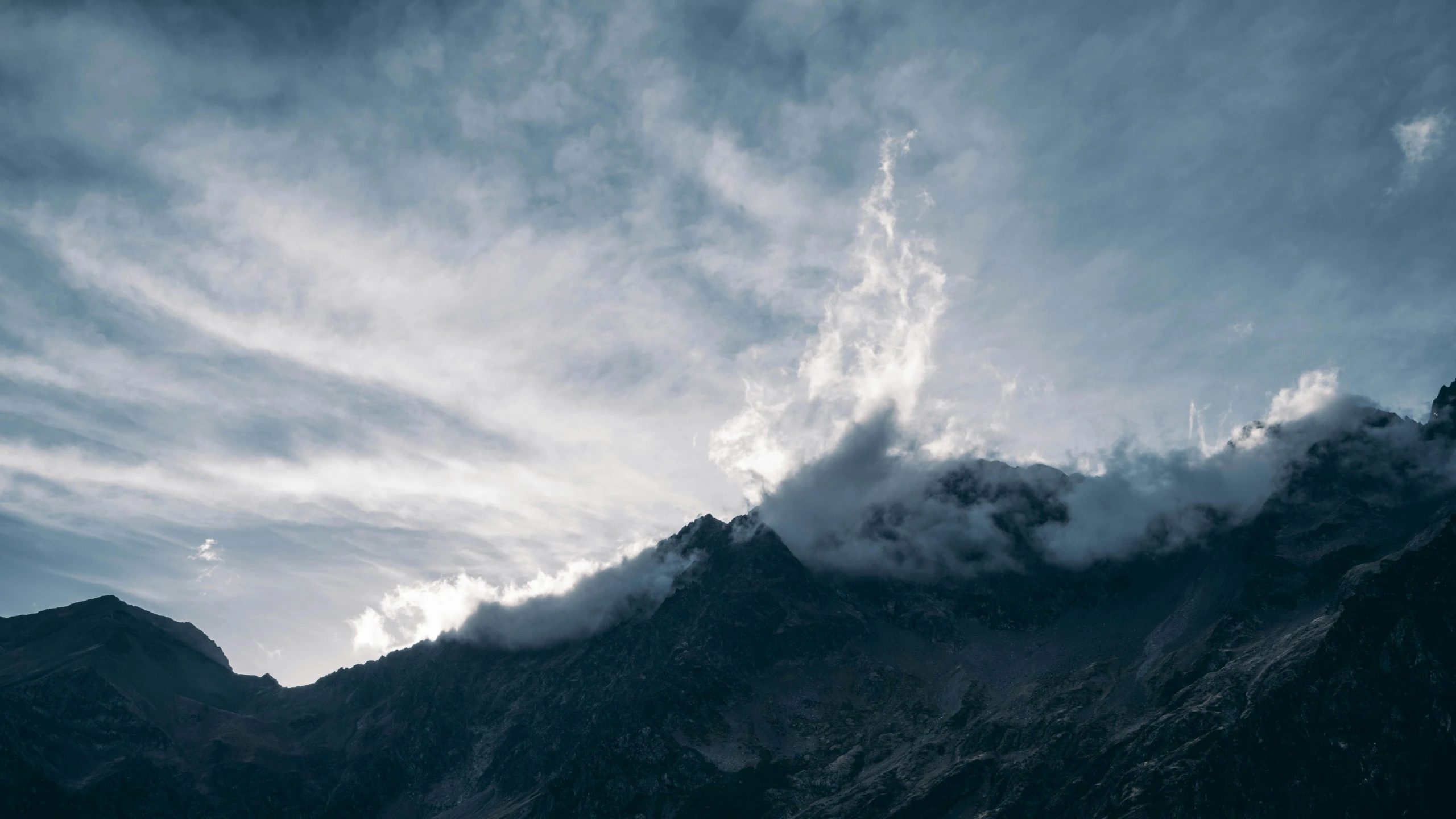 a mountain top with clouds rolling by and an airplane