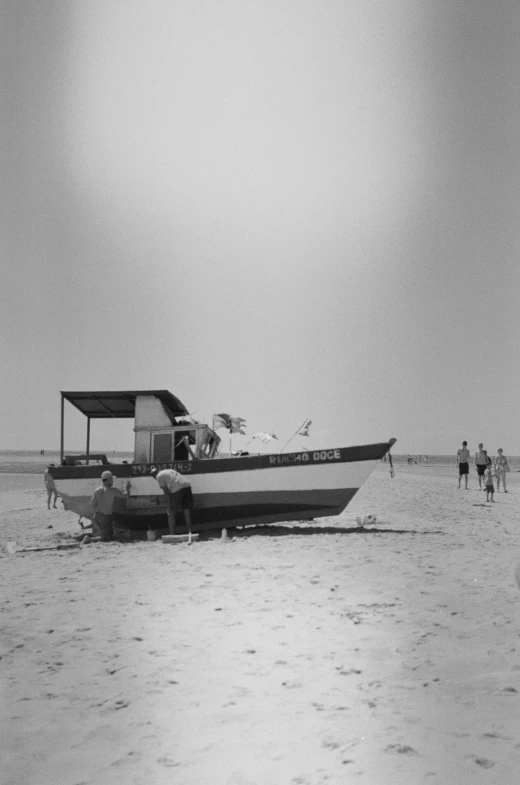 the water with several people standing in the distance and a boat tied to the shoreline