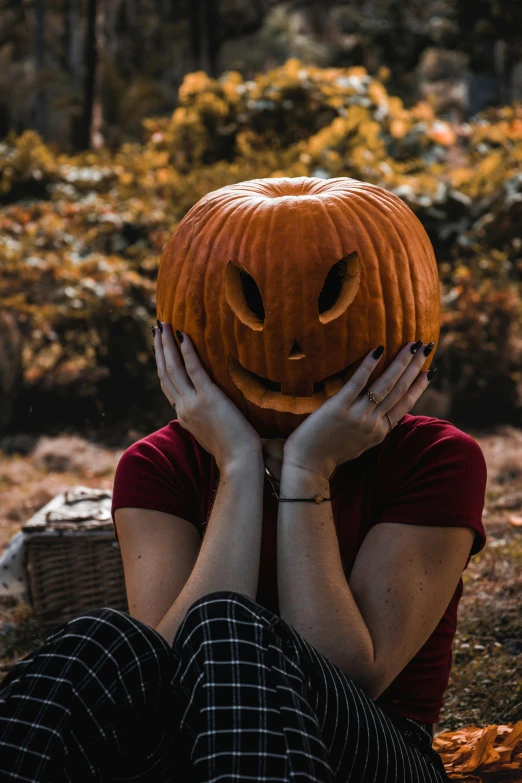 a woman hiding her face behind an pumpkin