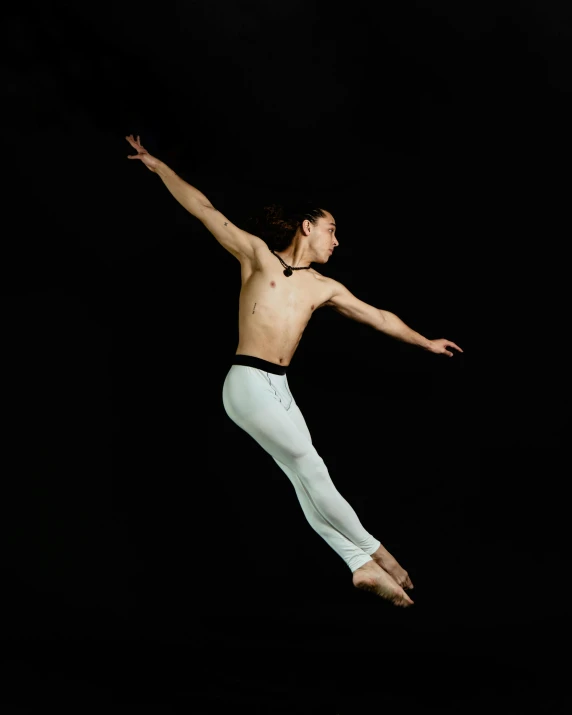 a man shirtless in a black t - shirt jumping in the air with his arms outstretched