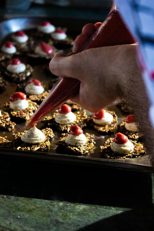 someone decorating a dish with red and white icing