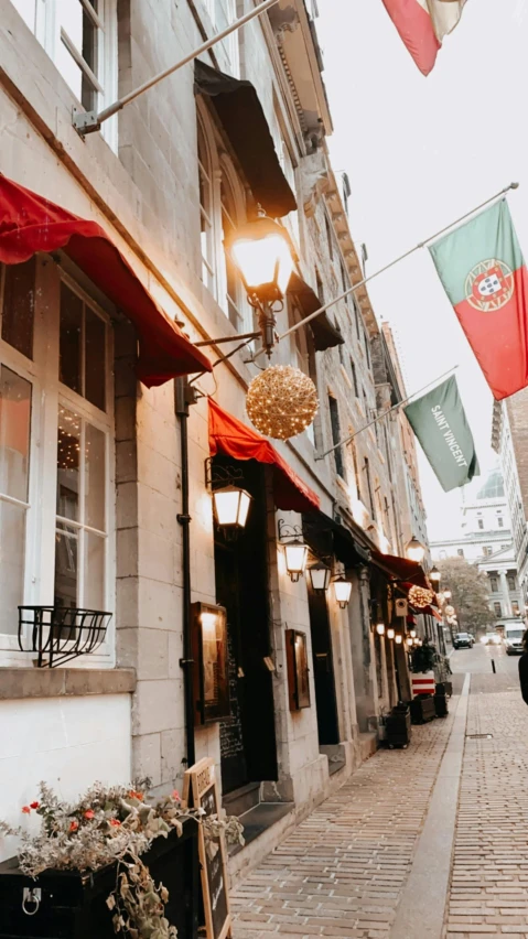 a narrow city street with shop lights and flags