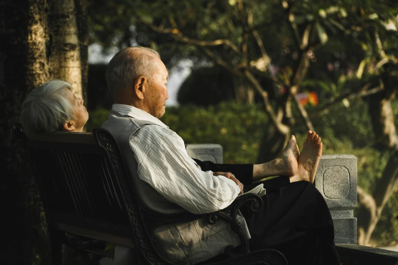 two older people sitting on park benches looking at trees