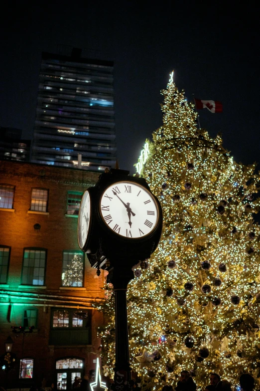 the clock is on top of a pole outside next to a christmas tree