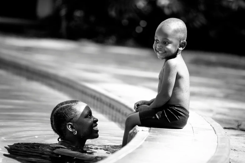 a small child smiles as he sits on the edge of a swimming pool