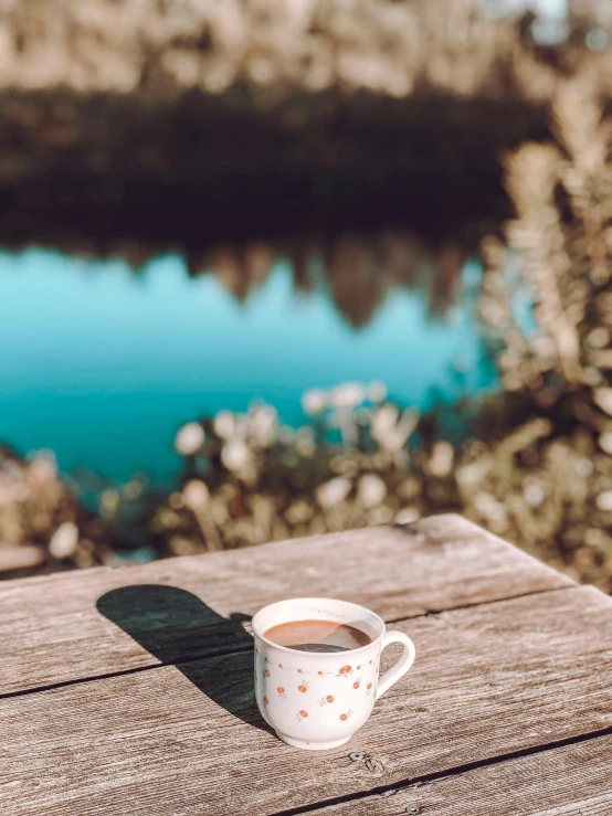 a cup of coffee on a wooden table overlooking a lake