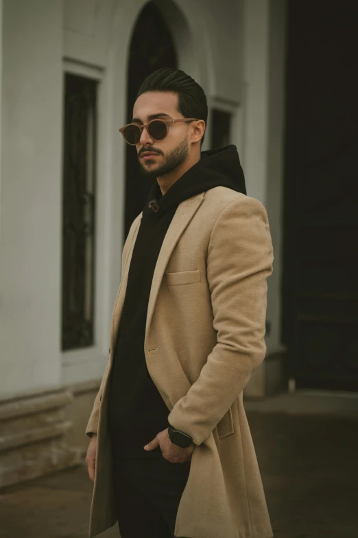 man in brown coat standing on sidewalk, wearing dark sunglasses