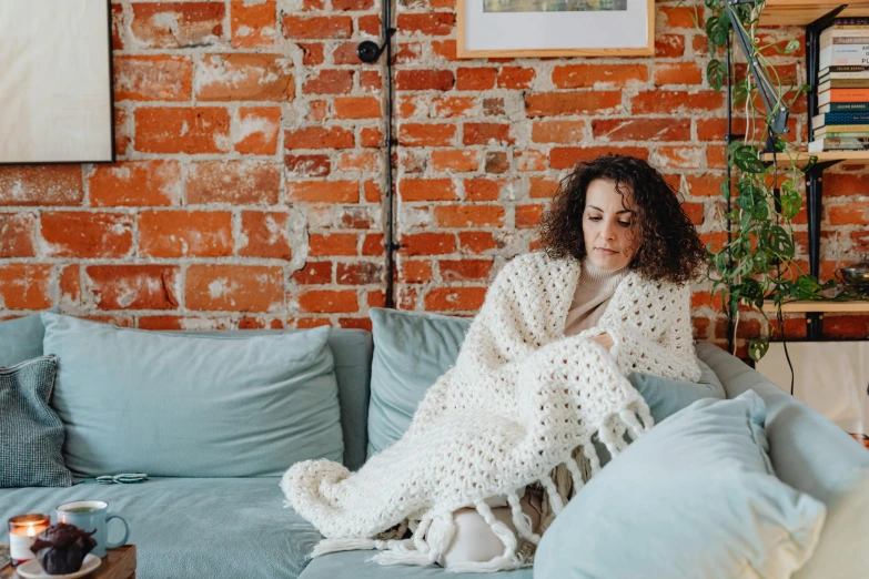 a young woman sits on a blue couch next to a large brick wall