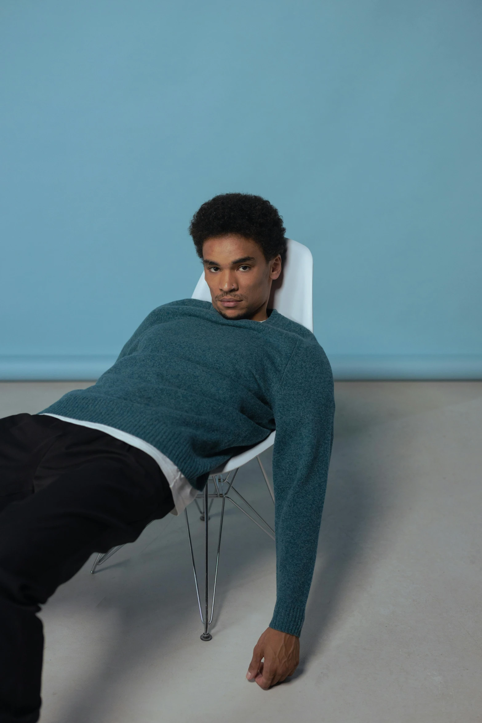 a young man with black pants and blue sweater seated on a chair