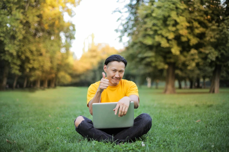 a man with a laptop computer is kneeling in the grass