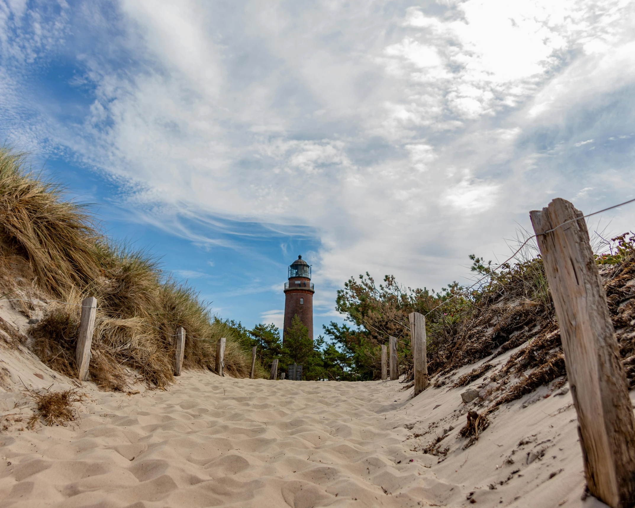 the lighthouse is standing on top of a beach by a fence