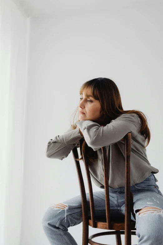 a woman sitting on a wooden chair with her head bowed