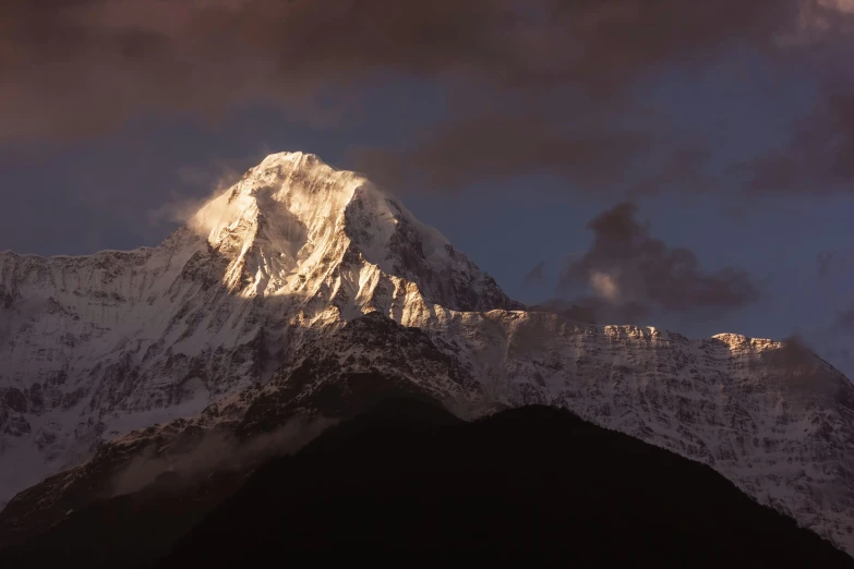 the top of a snow capped mountain with clouds hovering overhead