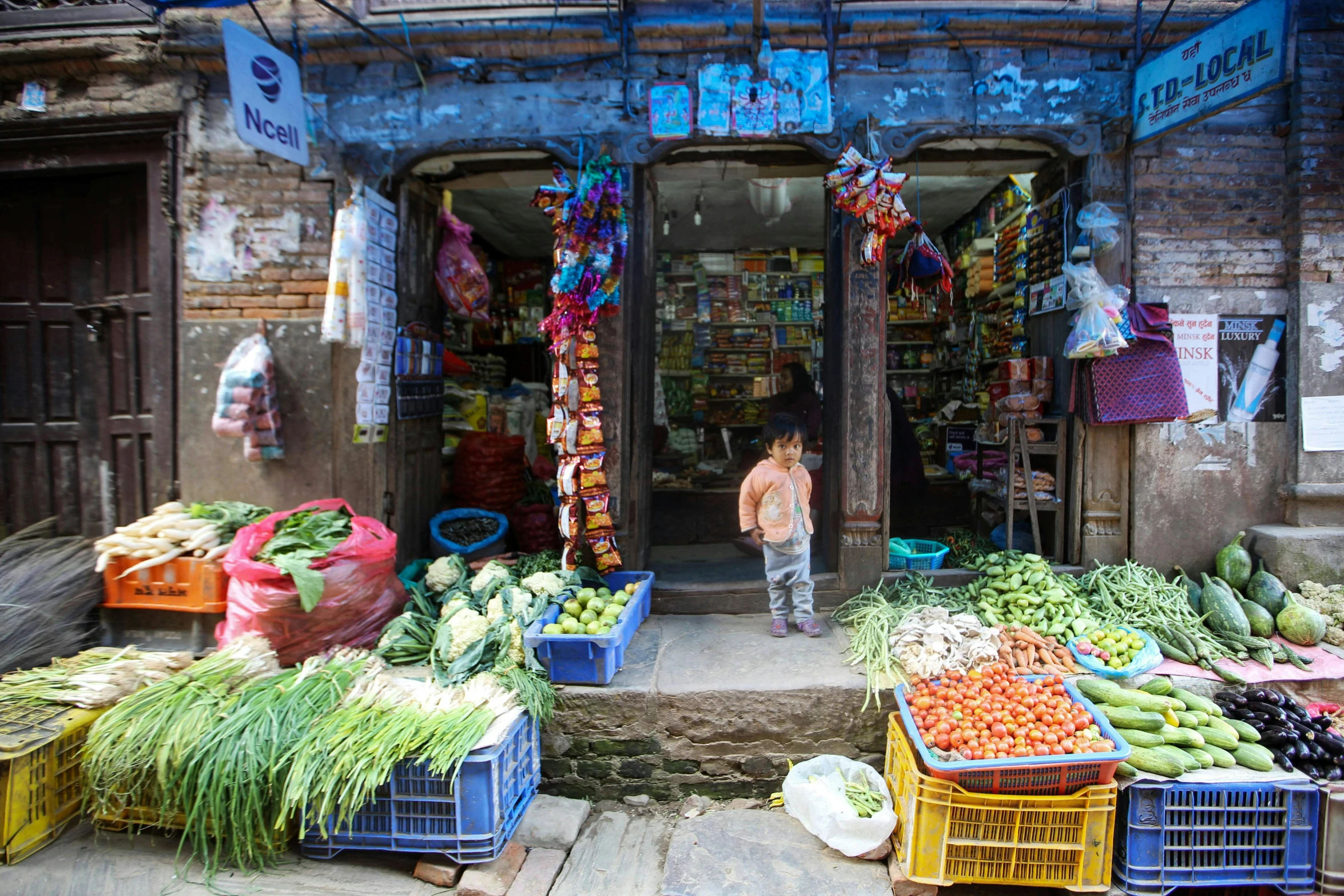 a woman is at the door of a store selling various fruits and vegetables