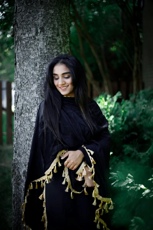 a woman in black standing by a tree with long black hair