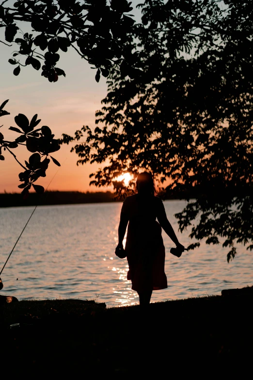 the silhouette of a woman at sunset walking near a lake