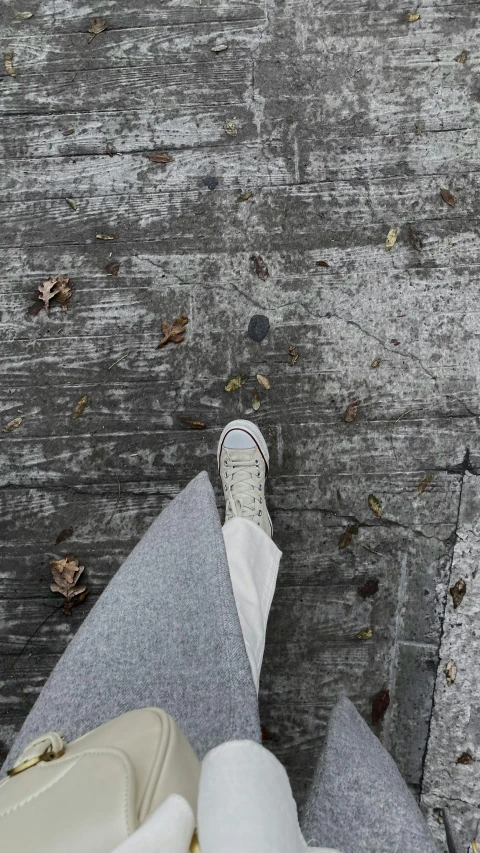 a person wearing sneakers standing on cement walkway with a bag on it