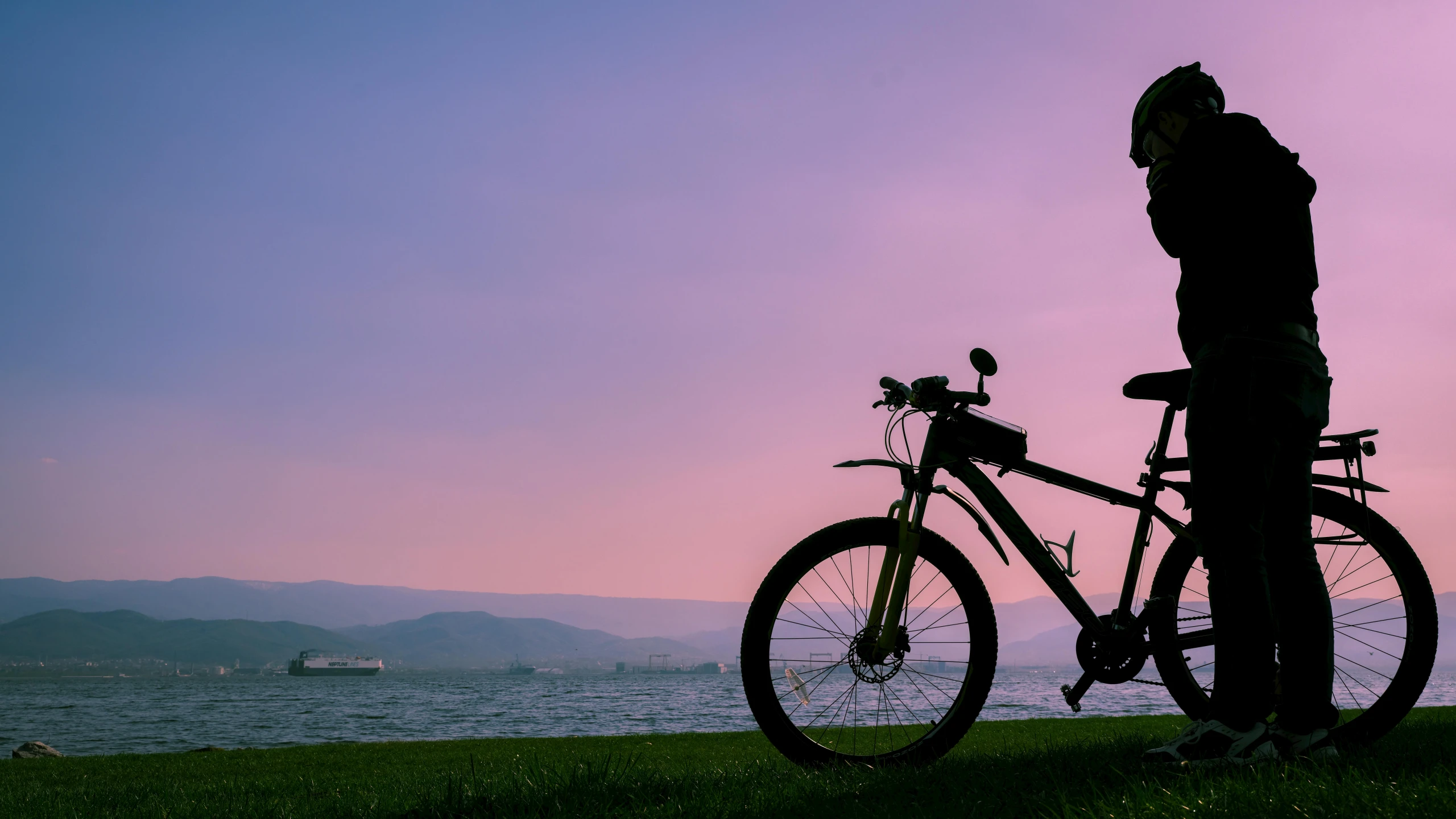 two men stand and look at a bike by the water