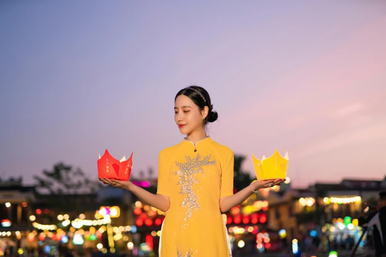 a woman is holding some small boxes and wearing a yellow dress