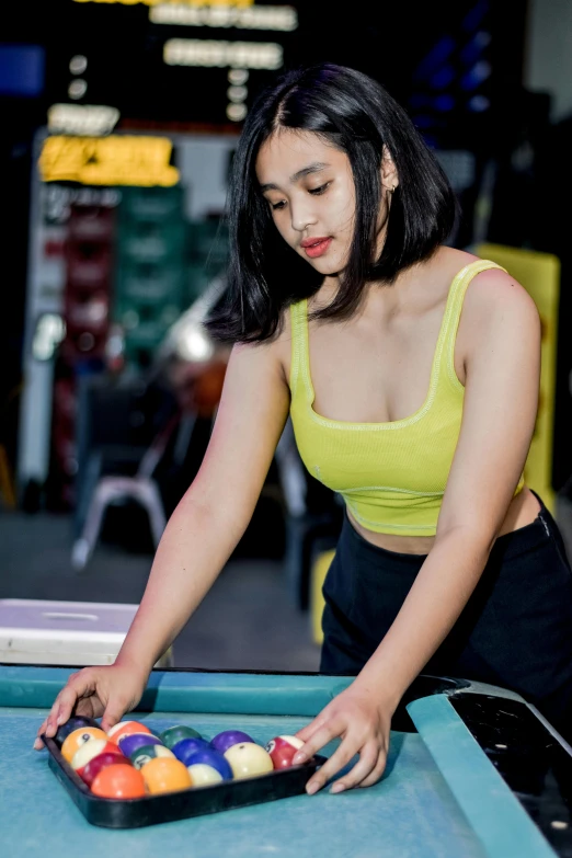 a girl in yellow top placing pool balls in a bowl