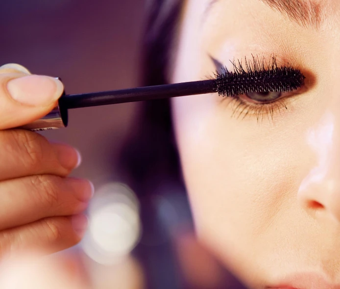 a woman getting ready for her eye makeup with a mascara