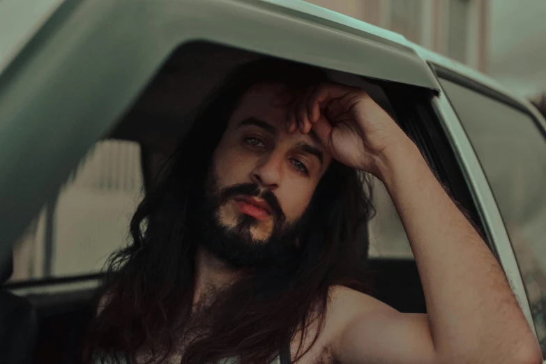 a man with long hair holding his head out the car window