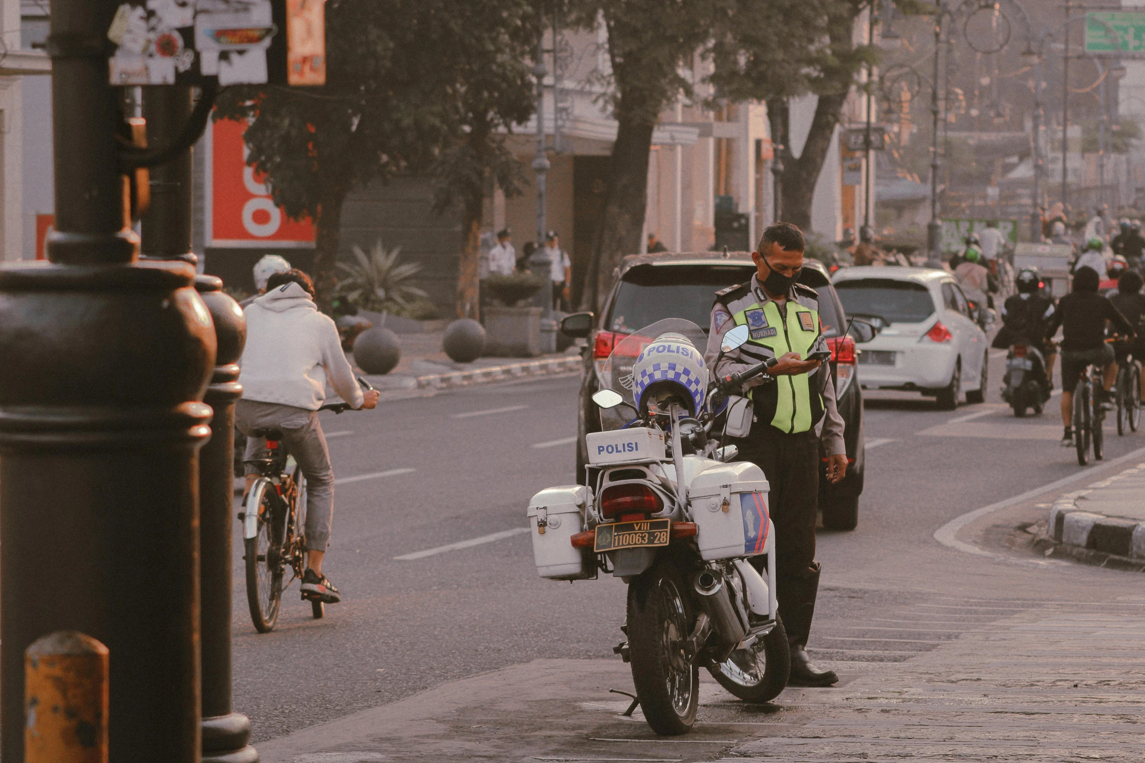 a man stands beside his motorcycle while people ride their bikes down the road