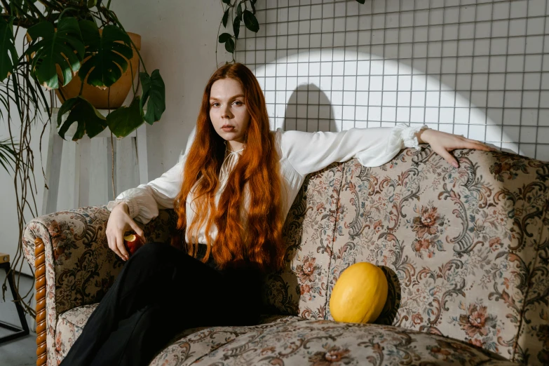 a woman is sitting on the couch near a plant