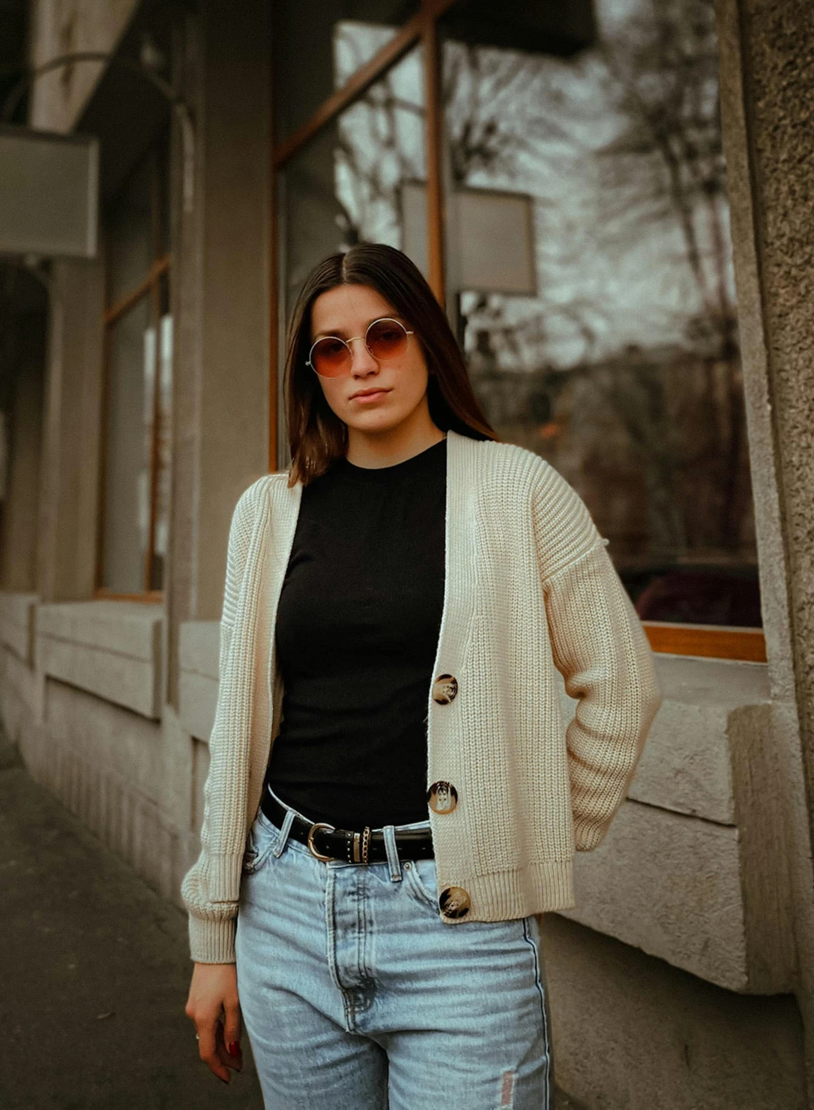 a woman standing outside in the sun with her hands in her pockets