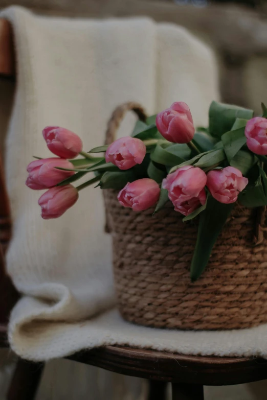pink flowers sit in a woven basket on top of a wooden chair