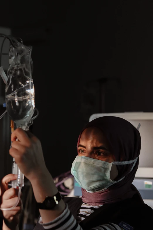 a woman wearing a surgical mask holding up a tube