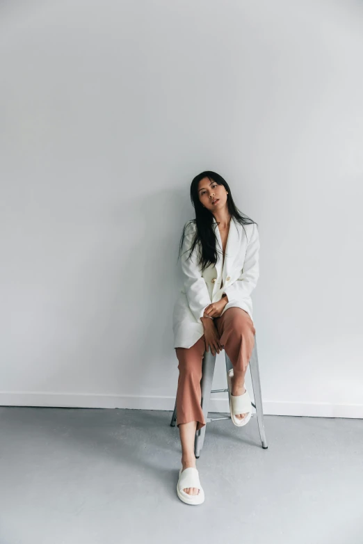 a woman sitting on a stool wearing white clothing