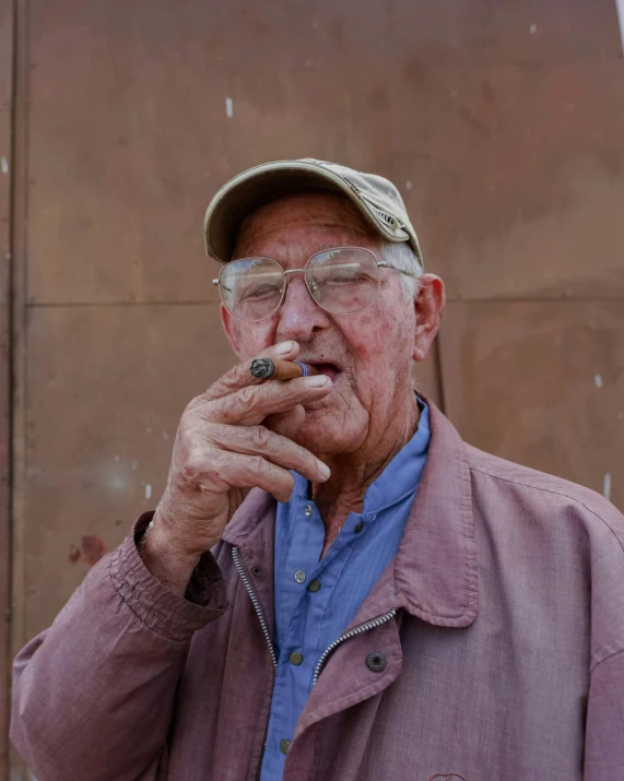 an old man smoking a cigarette and wearing a cap