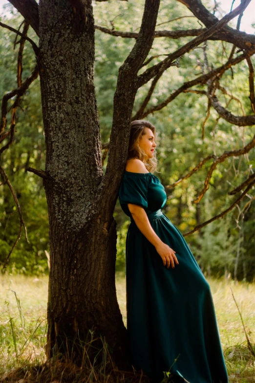 a woman in green dress leaning against tree