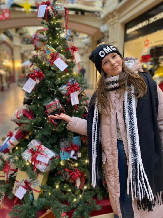 a girl standing near a christmas tree in a mall