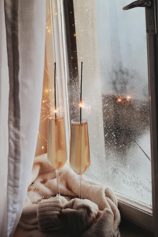 two wine glasses sit in front of a window and a blanket on the windowsill